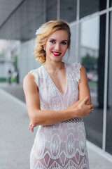 Beautiful blond bride in white wedding dress standing near mirror window outdoors.