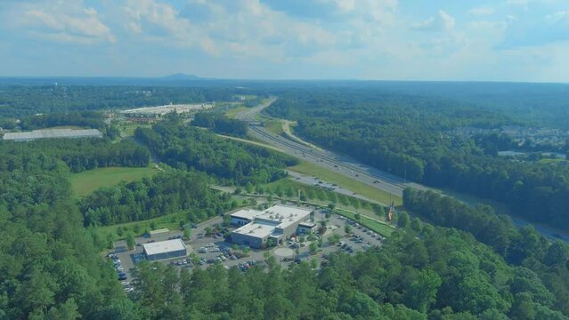 aerial footage of vast miles of lush green trees with buildings nestled in between and cars driving on the highway with powerful clouds and blue sky at Olde Rope Mill Park in Woodstock Georgia USA