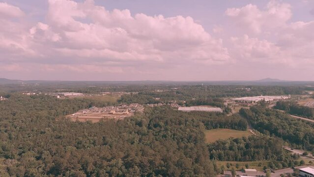 aerial footage of vast miles of lush green trees with buildings nestled in between and cars driving on the highway with powerful clouds and blue sky at Olde Rope Mill Park in Woodstock Georgia USA