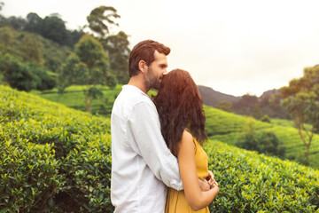 Romantic couple of travelers in love standing against nature background tea plantations landscape. Young adult brunette woman and man in front of perfect natural backdrop near Nuwara Eliya tea farm