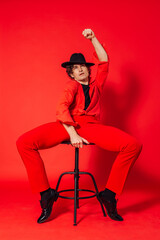 Fototapeta na wymiar Tall handsome man dressed in red shirt, trousers and black hat posing on the red background