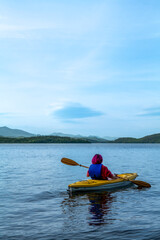 Woman kayaking. Rear view of a young man splashing water while kayaking on the river with mountains background. High-quality photo