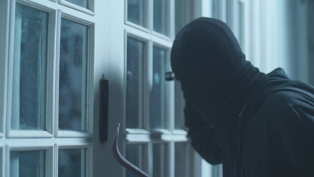 Close Up Of Thief Man Holding Flashlight And Crowbar Looking Inside The House While Standing Outside In The Dark Night
