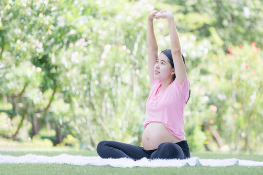 Happy pregnant woman sitting relax in the park and stretching muscles