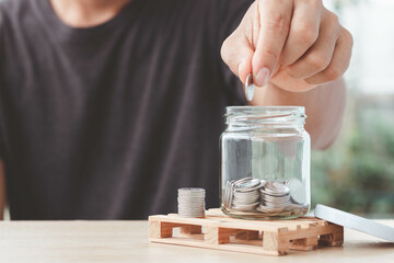 Coins in a glass bottle, Hand of male or female putting coins in jar with money stack step growing growth saving money on nature background, Concept finance business investment.