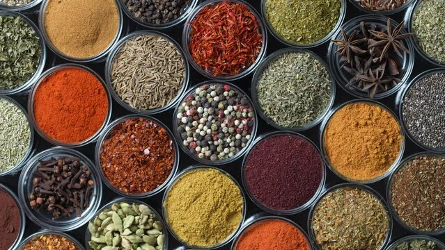 Assortment of aromatic spices, seeds and dry herbs for cooking food on background rotating in smal glass bowls rotating, close up, top view