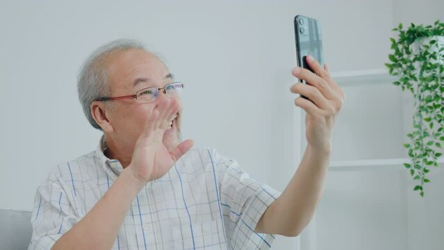 The old man sitting on the sofa using a smartphone video call, old man chatting with a child over video accompaniment happily laughing smiling at home on vacation