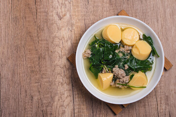 Vegetable gourd soup with minced pork and egg tofu in white bowl on wooden background Thai food.(gaeng jued tum luang)