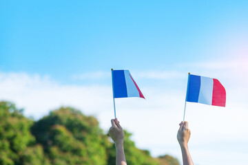 hand holding France flag on blue sky background. holiday of French National Day, Bastille Day and...