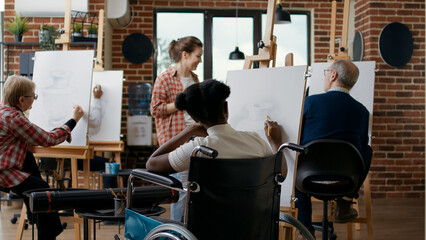 Young woman with disability learning to draw sketch on canvas, attending art class lesson with...