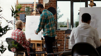 Modern artist analyzing vase drawing by senior woman in art school lesson, teaching imagination skills to draw creative model and design on canvas. Artistic sketch. Tripod shot.