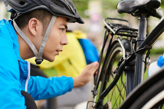 Frowning cyclist in protective tuve helmet checking bicycle wheels before ride