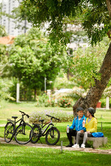 Happy young Vietnamese couple drinking fresh water under tree in park after bicycle ride