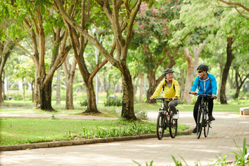 Happy boyfriend and girlfriend riding bicycles in city park when training for competition
