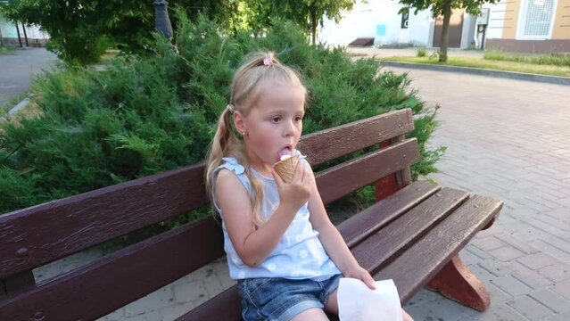 Little cute girl with an ice cream sitting on the bench in the park, soft focus background