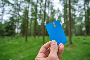 hand holding a blue credit card in the forest.