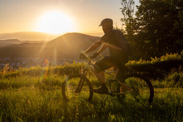 Mountainbiker in der tiefstehenden Abendsonne blickt auf die kleine Stadt Dahn im Pfälzerwald