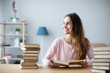 Happy student girl at a table with bunch of books is studying. Education.