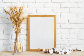 Vase with ears of wheat and photo frames against brick wall