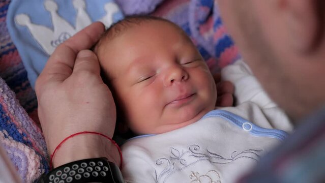 Close-up portrait of a newborn baby in the hospital. Father gently strokes the head of his newborn son.