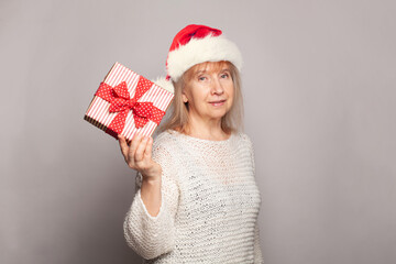 Senior woman wearing Santa Claus hat holding Christmas gift with red ribbon. Mature female...