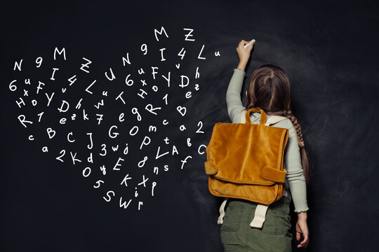 Small child girl in school uniform writing letters on a black chalkboard