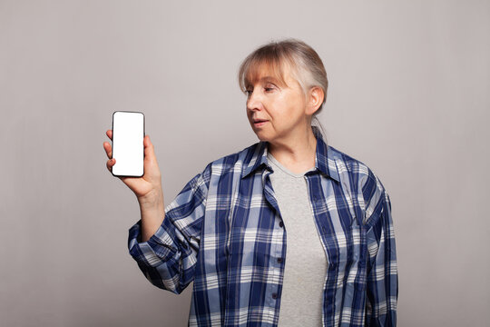 Mature woman holding smartphone with empty display for advertising and product placement