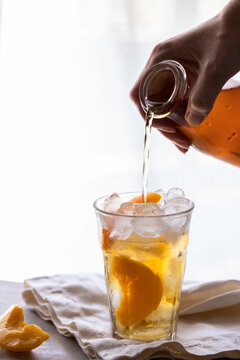 Hand hlding bottle and poring peach ice tea into the glass on the hablebackground