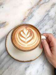 top view hand holding a cup of cappuccino or latte coffee on table