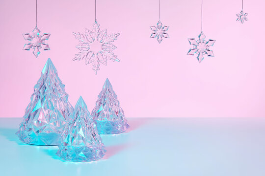 Abstract surreal Winter scene with Christmas decorations made of crystal glass. Xmas trees and snowflakes on holographic pink background with copy space, front view.
