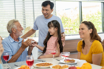 Happy family gathering enjoying having lunch together at home. Child daughter celebration around dining table with parents, grandparents and multi-generation family
