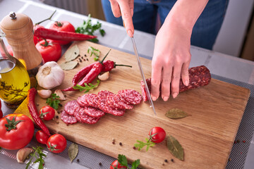 woman's hands cutting a salami sausage on wooden cutting board at domestic kitchen