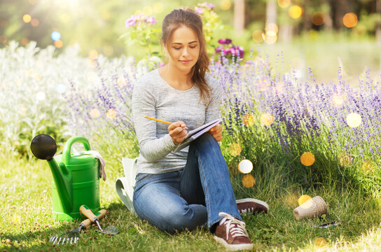 gardening and people concept - young woman writing to notebook at summer garden