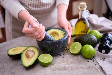 making guacamole - woman holding pestle to crush avocado in marble mortar on grey concrete table
