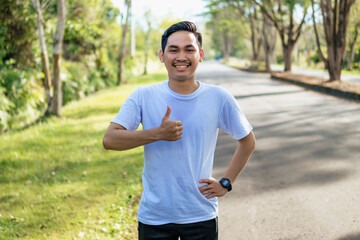Cheerful young Asian man showing thumbs up gesture in the nature. Healthy lifestyle