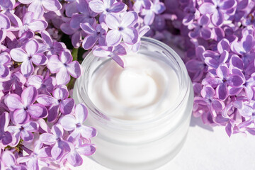 mockup of white frosted glass jar for branding with cosmetics - cream, gel, skin care. Cosmetic bottle container and lilac flowers on white background.