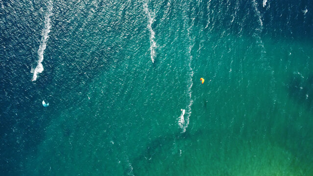 Aerial drone view of windsurfers and kite surfers enjoying on blue sea ocean waves..