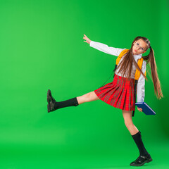 Cute happy schoolgirl in uniform and glasses, walking on green background. child with backpack and...
