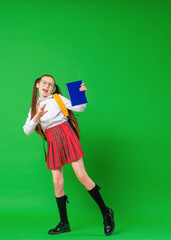 Cute happy schoolgirl in uniform and glasses, walking on green background. child with backpack and...