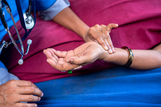 Close shot of doctor checking pulse rate to sick women by holding hands at hospital - concept of treatment, routine and medical.
