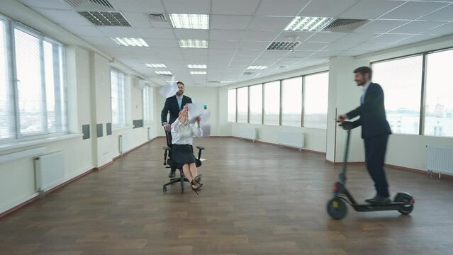Fooling around, office workers rejoice at successful completion of the project, a man rides a female colleague's on an office chair, flying papers, positive emotions.