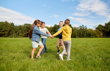 childhood, leisure and people concept - group of happy kids playing round dance at park