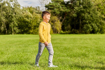 childhood, leisure and people concept - happy boy walking on lawn at park