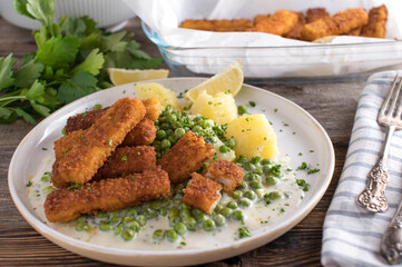 Fish sticks with peas, boiled potatoes and bechamel sauce on a plate