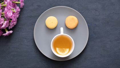 Smile with macaroons and cup tea on a plate on a dark stone table with flowers. Beautiful delicious dessert