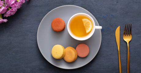 Smile with macaroons and cup tea on a plate on a dark stone table with flowers. Beautiful delicious dessert