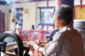 お寺でお香を焚いている中国人の高齢者男性 - obrazy, fototapety, plakaty
