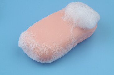 Pink soap with white foam bubbles on blue background.	