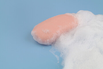 Pink soap and foam on blue background, room for text.	