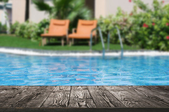 Empty wooden surface near outdoor swimming pool with clear water. Space for design